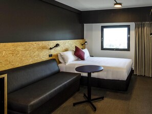 A hotel room with a bed, a small round table, a sofa, and a window with curtains. - ibis budget Sydney East (Darlinghurst)