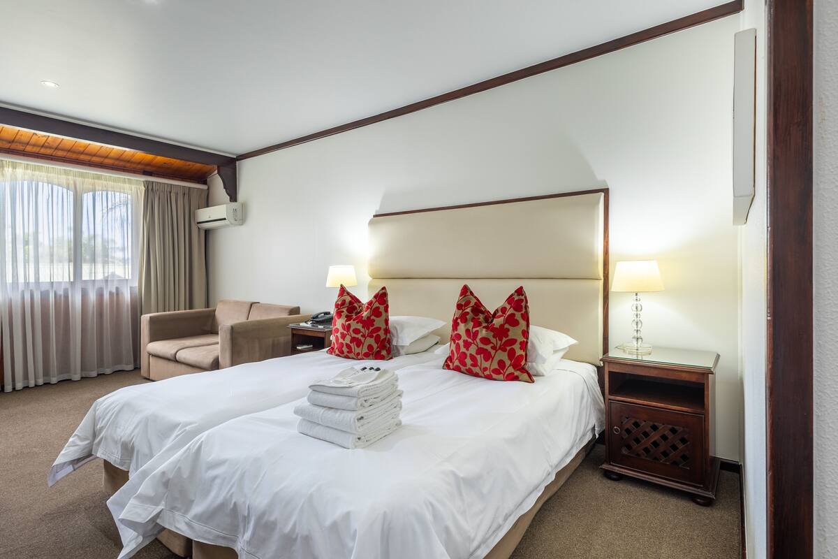A hotel room with two beds, a sofa, a nightstand, and a lamp.