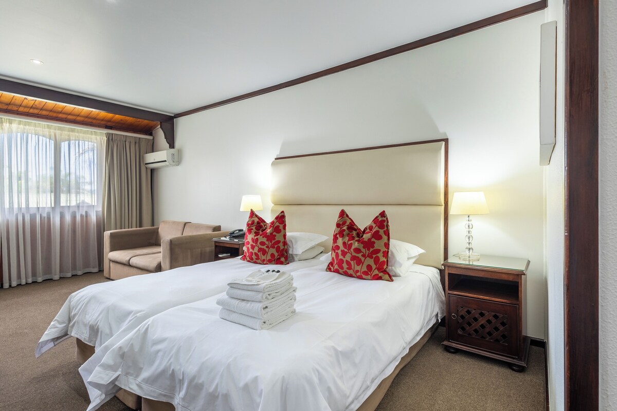 A hotel room with two beds, a sofa, a nightstand, and a lamp.