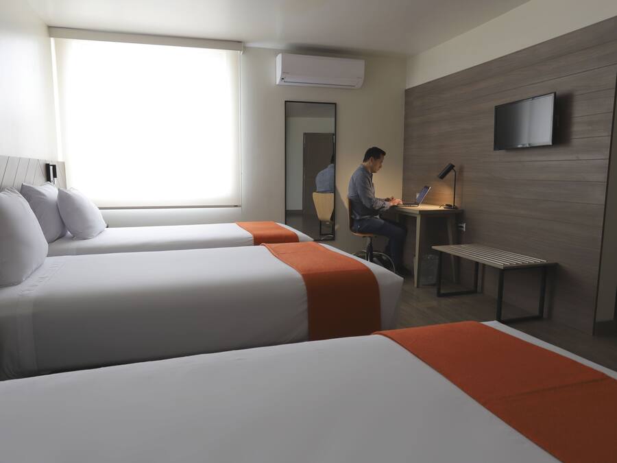 Una habitación de hotel con dos camas, un escritorio, una silla, un televisor y un equipo de aire acondicionado.