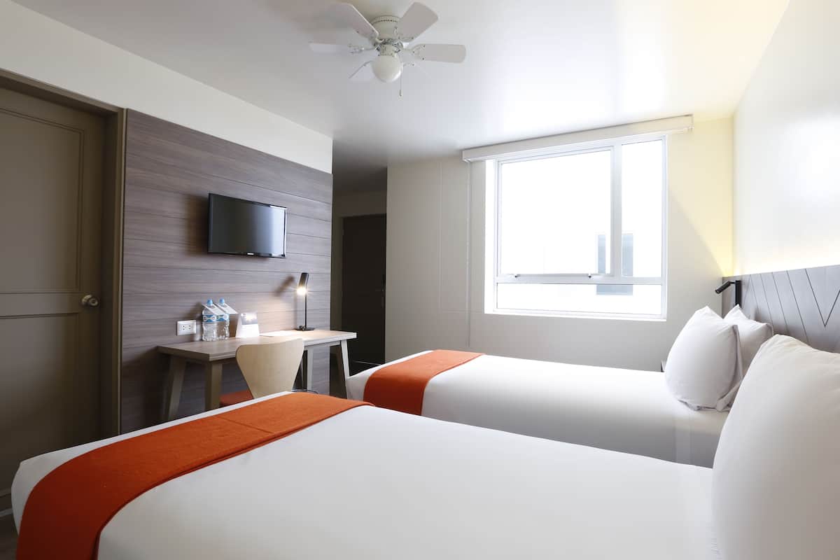 Une chambre d’hôtel avec deux lits, un bureau, une télévision et une fenêtre.