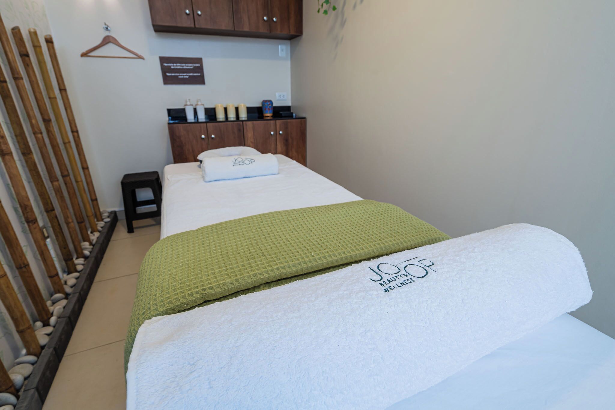 A neatly arranged room with a bed, a small stool, a wooden cabinet, and a wall-mounted towel rack.
