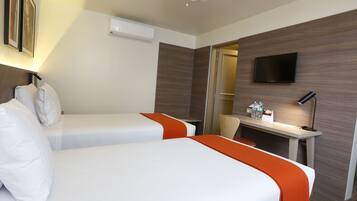A hotel room with two beds, a desk, a TV, and a ceiling fan.