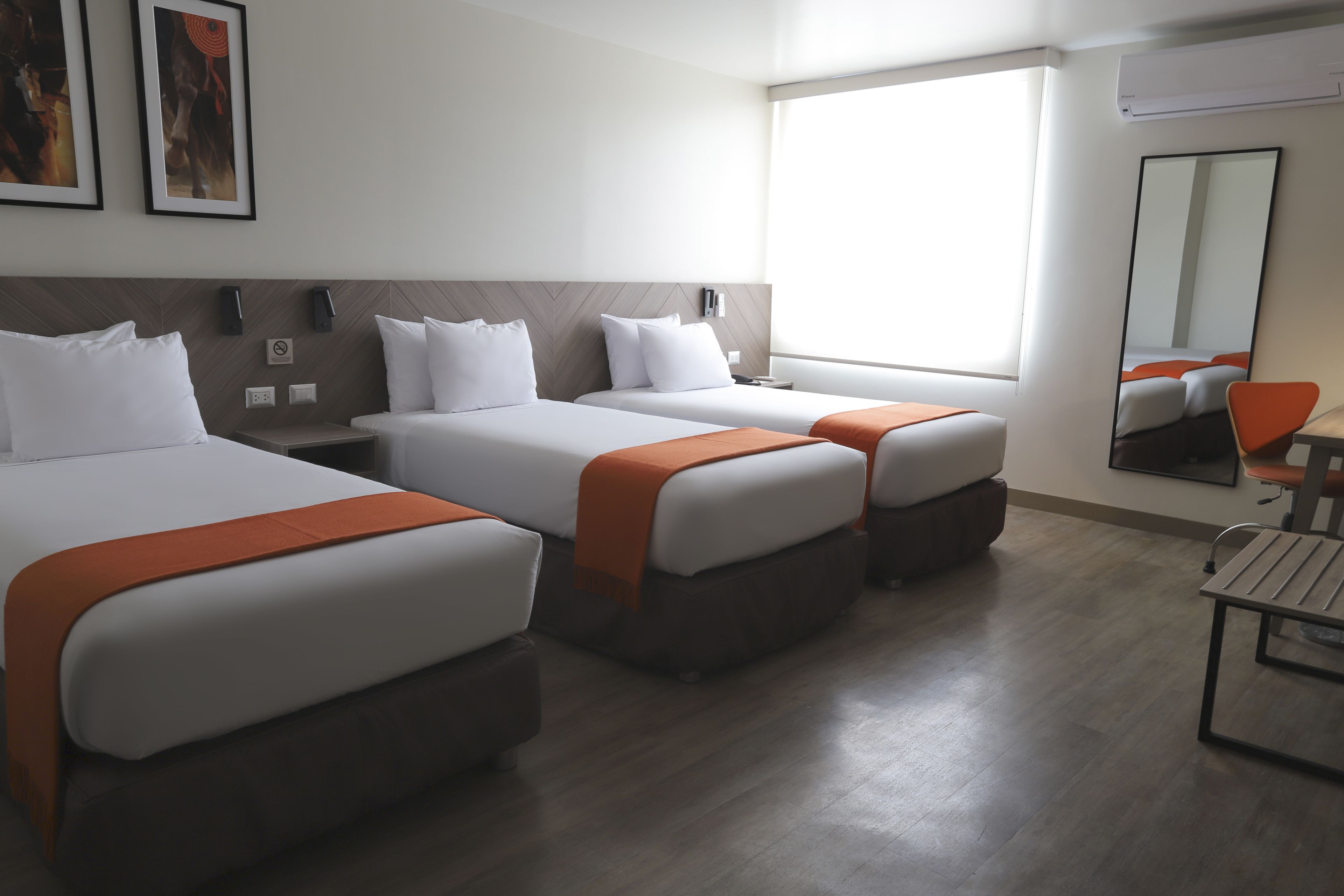 Habitación de hotel con dos camas, un ventanal grande, un espejo y una mesita.