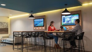 Een moderne vergaderruimte met een lange tafel, zwarte stoelen en twee grote schermen waarop sportevenementen worden getoond.