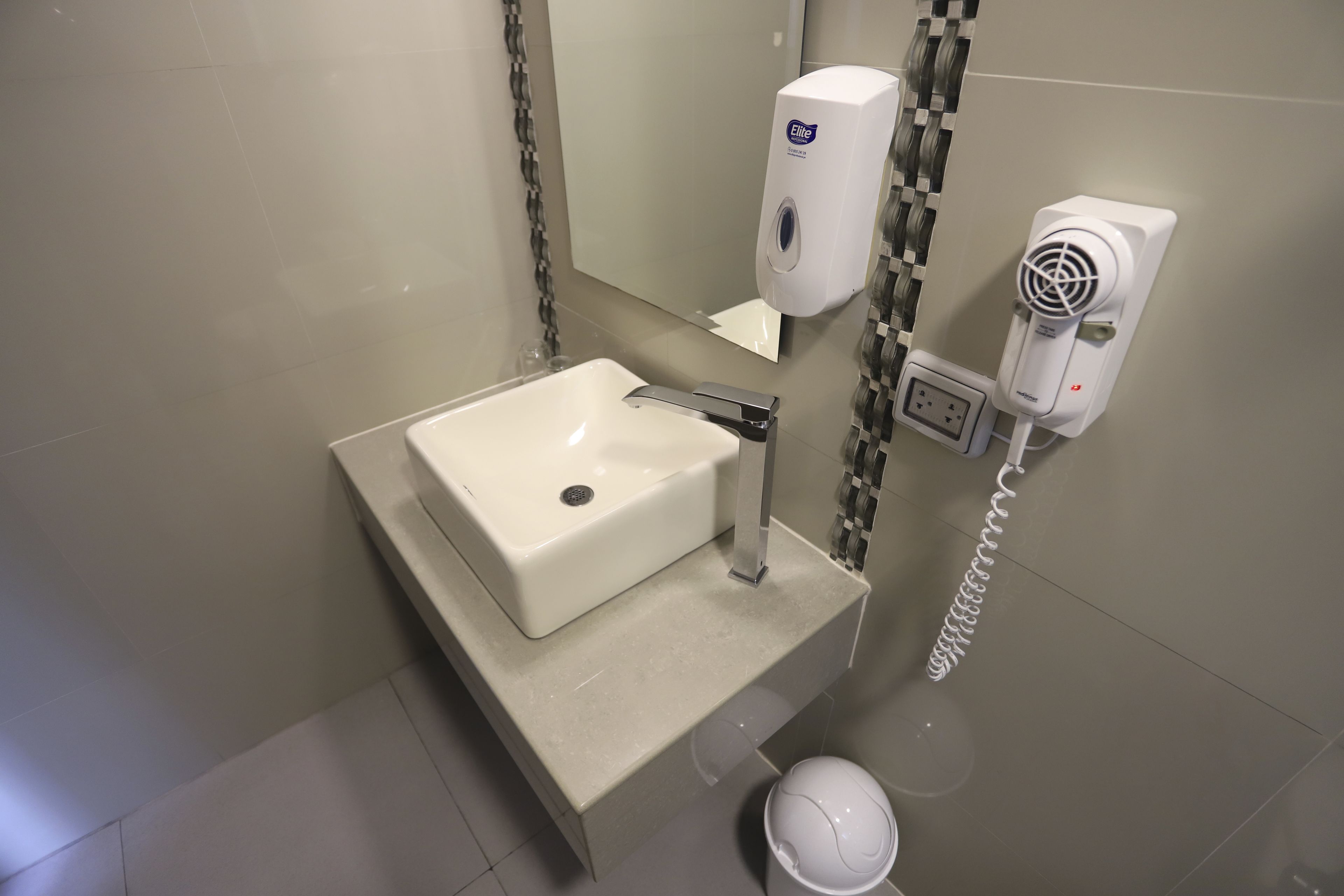 A bathroom with a white sink, a mirror, a hand soap dispenser, and a hair dryer.
