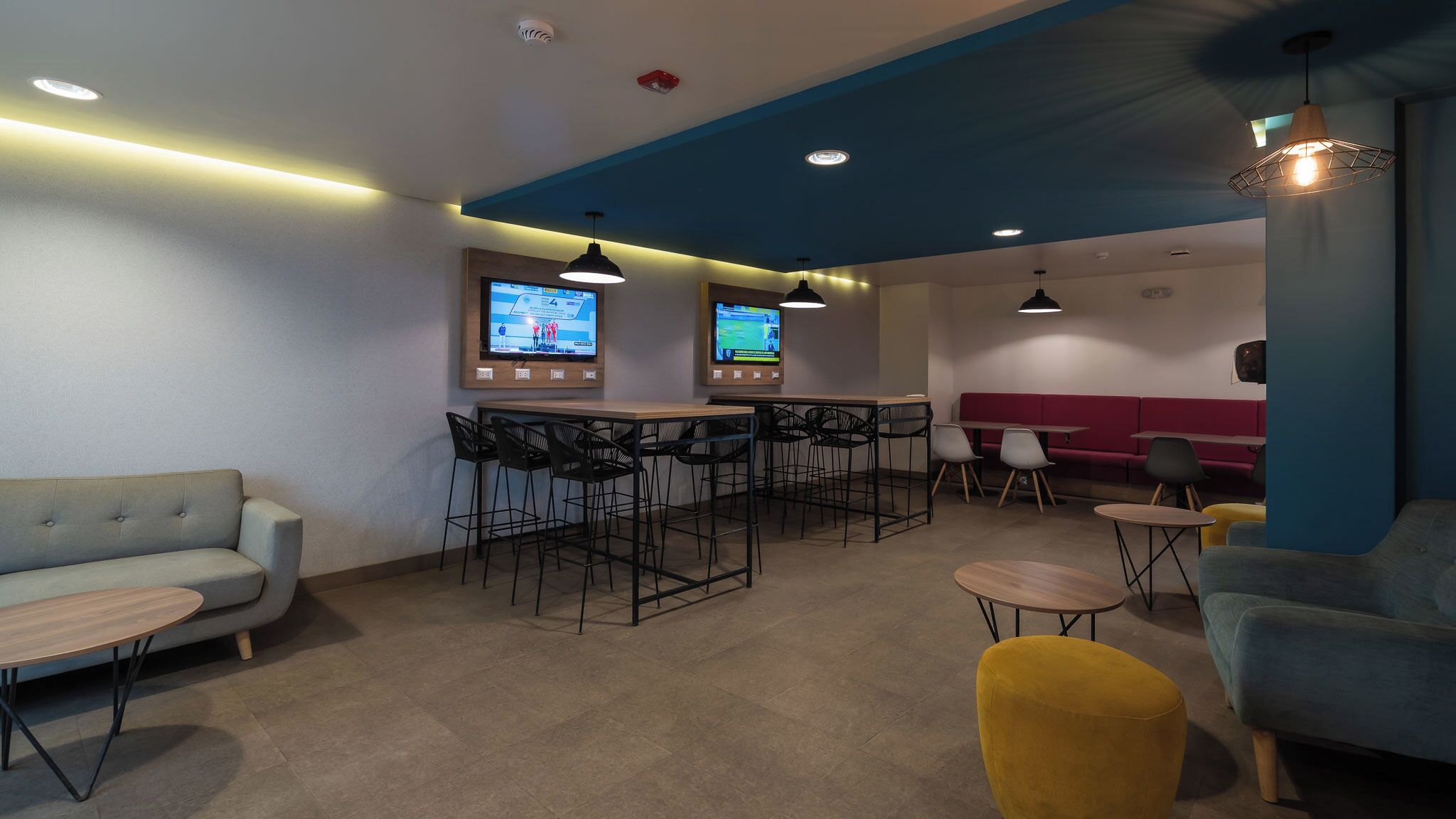 A modern lounge area with a bar, seating, and two screens displaying content.