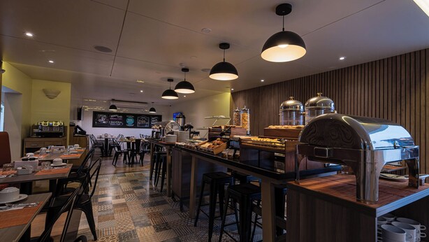 Een modern café met een centrale bar, een zithoek en een koffiehoek.