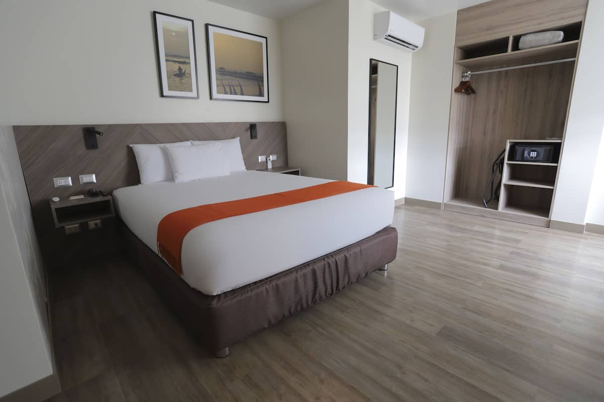 Une chambre d’hôtel moderne avec un grand lit, une tête de lit en bois, une armoire et un tableau encadré au mur.