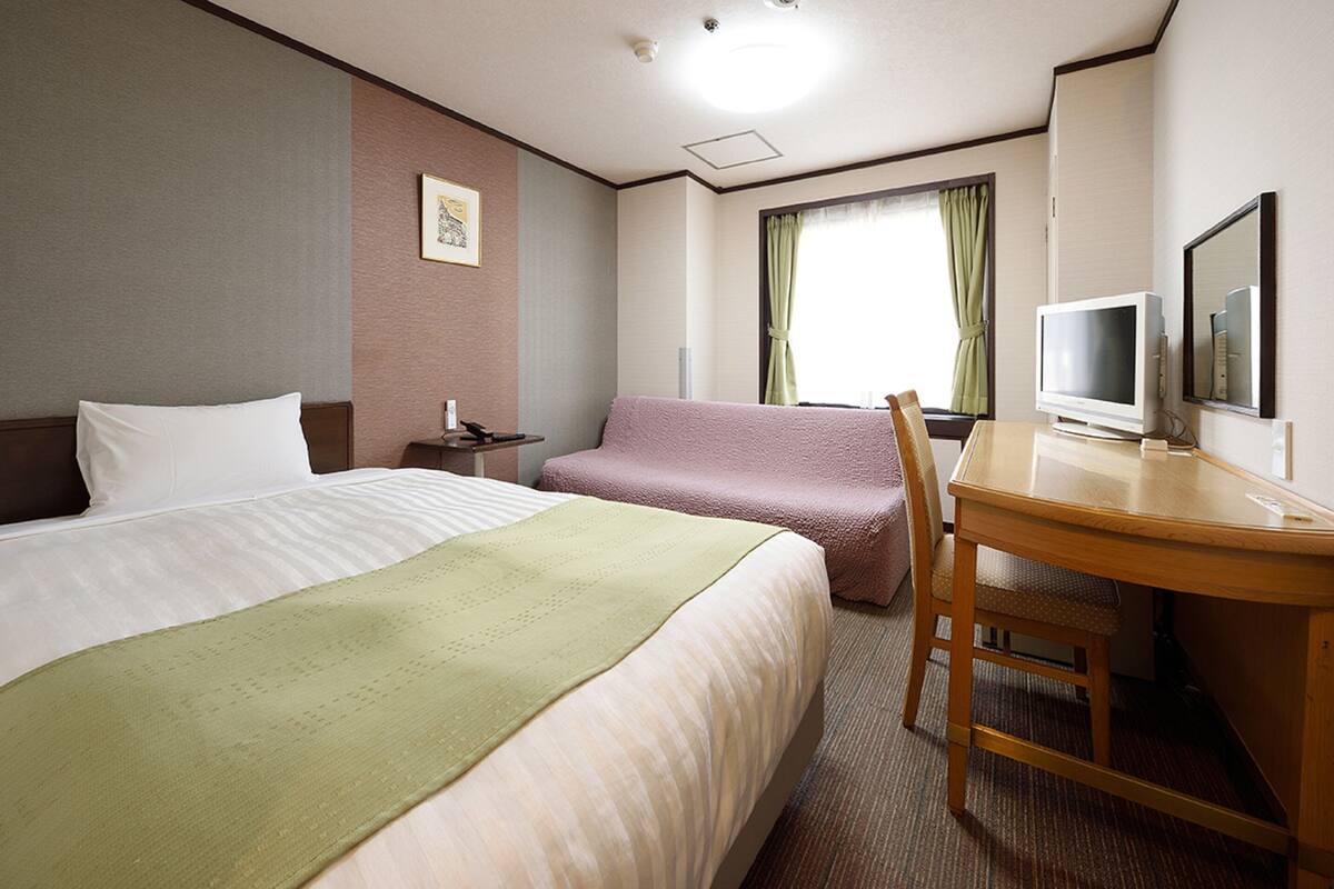 A hotel room with two beds, a desk, a chair, a television, and a window with curtains.