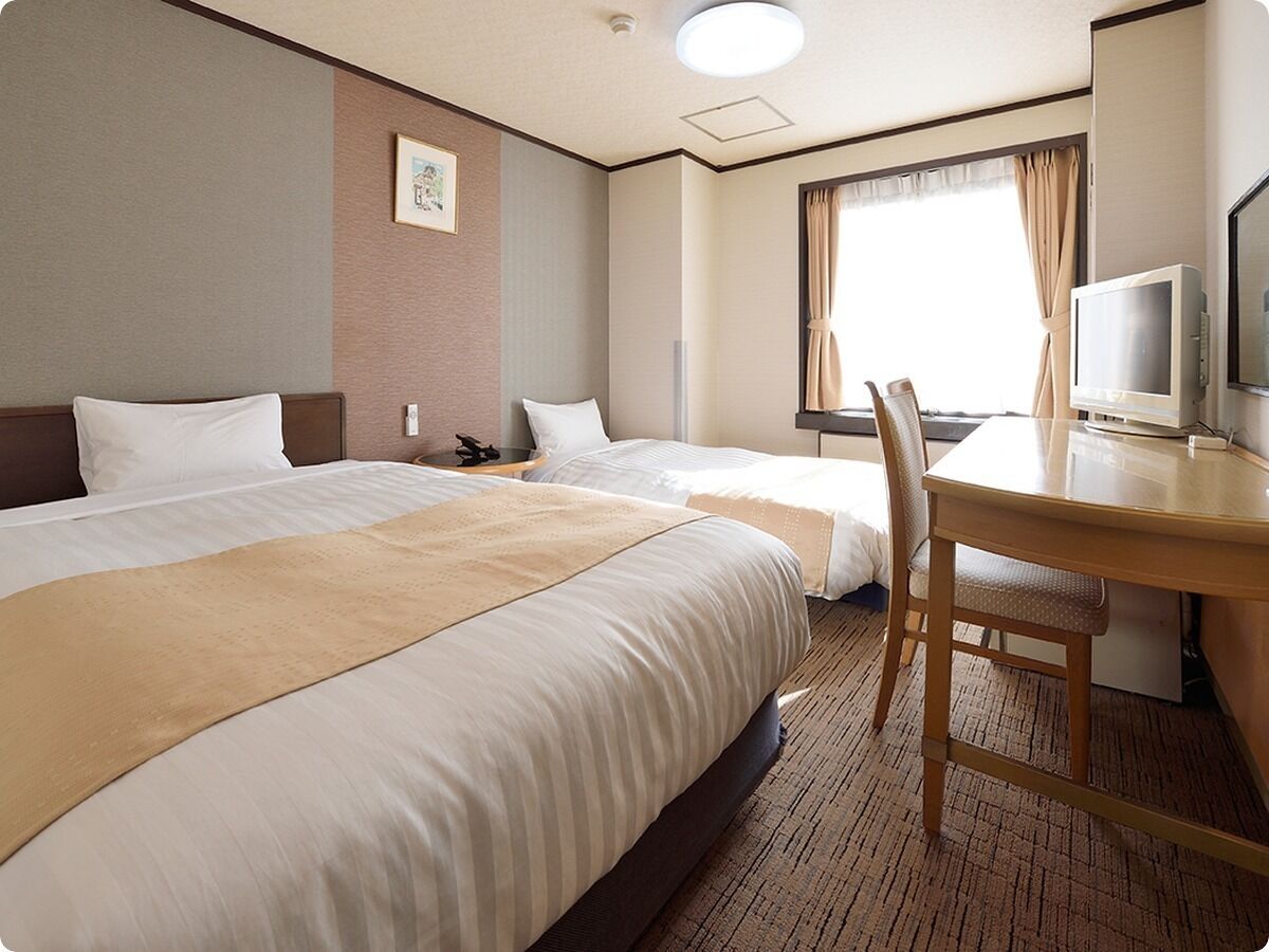 A hotel room with two beds, a desk, a chair, a television, and a window with curtains.
