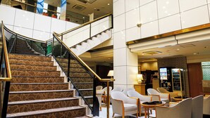 A spacious lobby with a central staircase, seating area, and a high ceiling with skylights.