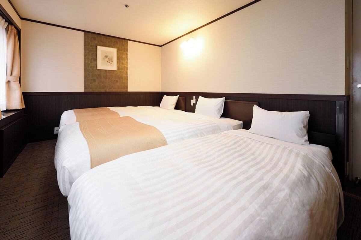 A hotel room with two beds, a wooden headboard, a wall-mounted light, and a framed picture.