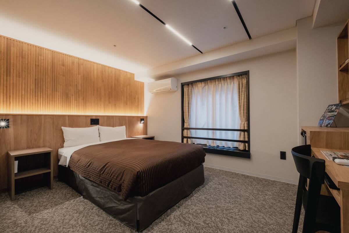 A modern hotel room with a large bed, bedside tables, a desk, and a window with curtains.