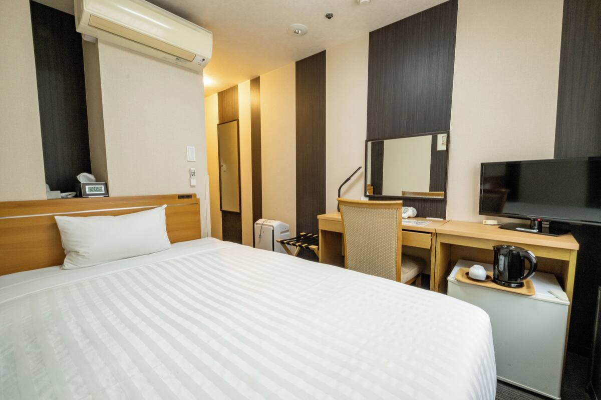 A hotel room with a bed, desk, chair, television, and a coffee maker.
