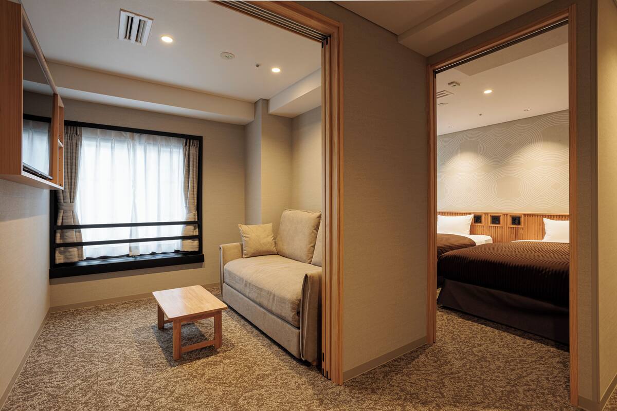 A hotel room with a sofa, a small table, a bed, and a window with curtains.