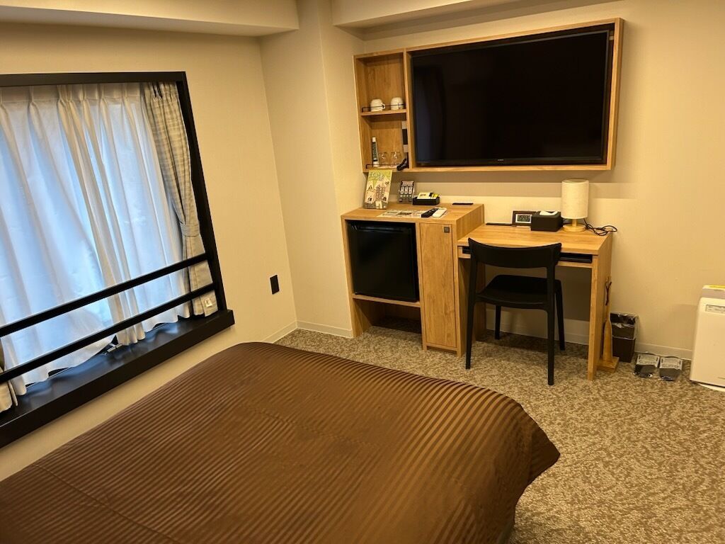 A hotel room with a bed, a desk, a chair, a television, and a window with curtains.