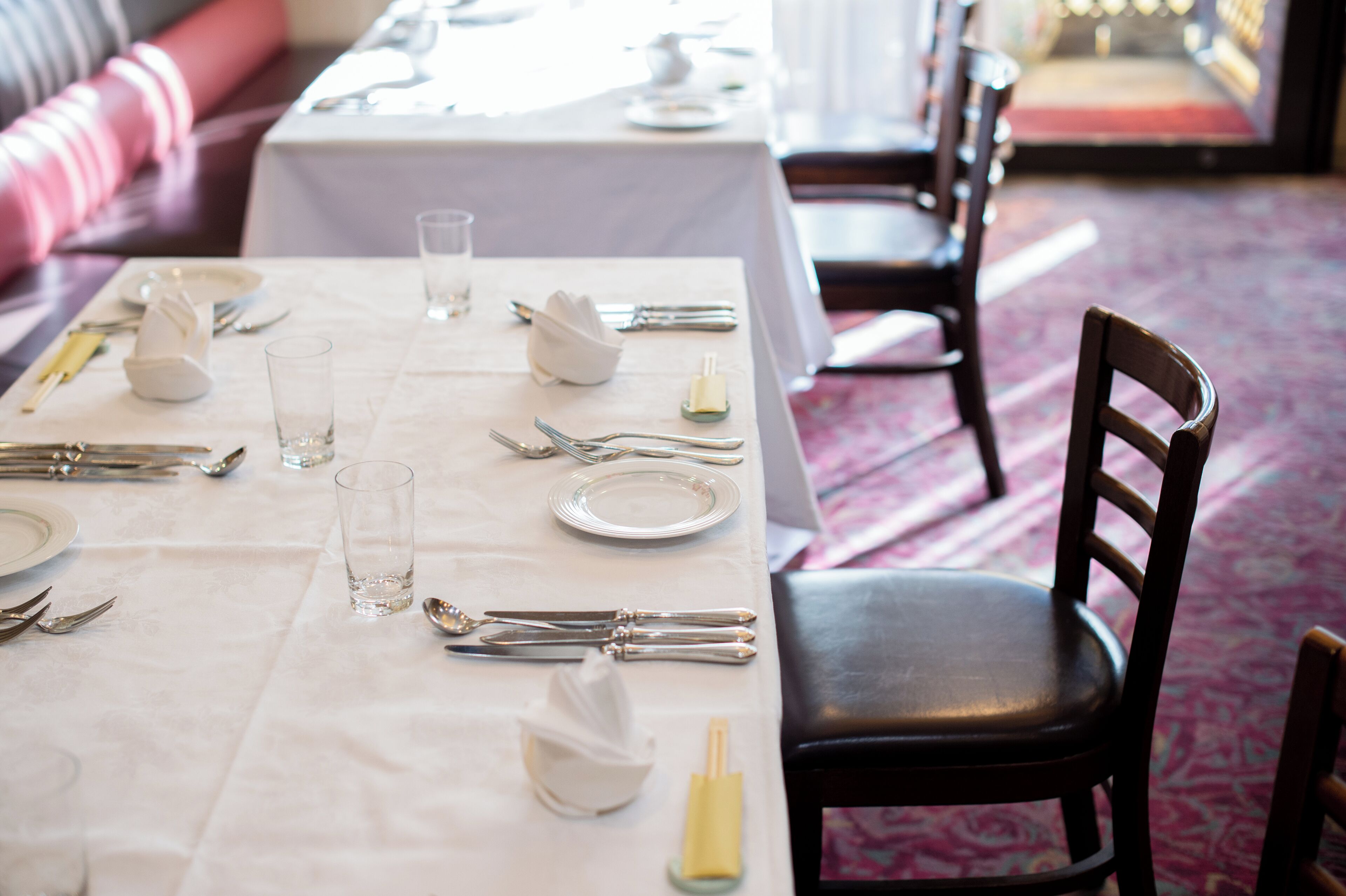 A dining table set with white tablecloth, silverware, plates, and glasses.