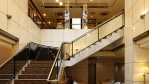 A spacious lobby with a grand staircase, comfortable seating areas, and a high ceiling with natural light.