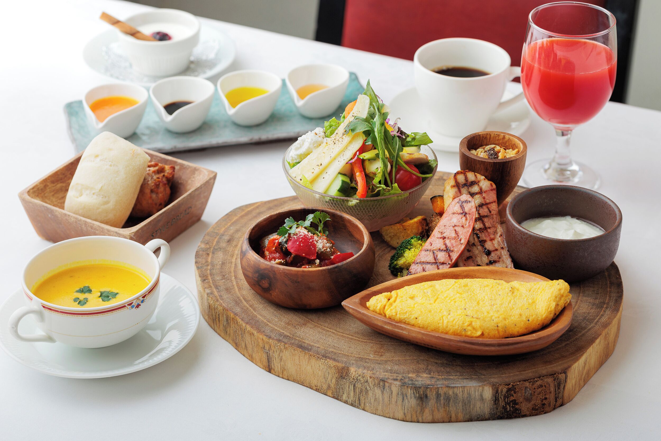 A variety of dishes including soup, salad, grilled meat, and an omelette on a wooden board.
