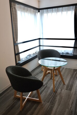 A corner room with a glass table and two chairs, a large window with curtains, and a view of a building outside. - Tokyo Asakusabashi Belmont Hotel (Tokyo)
