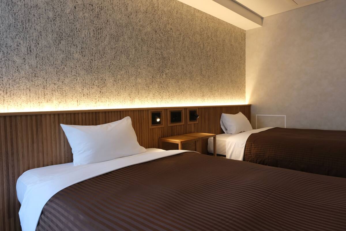 A hotel room with two beds, a wooden headboard, and a textured wall.