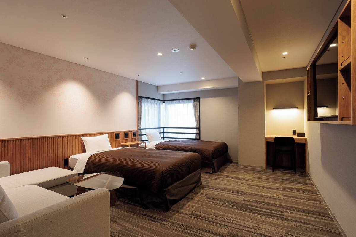 A hotel room with two beds, a desk, a chair, and a sofa.