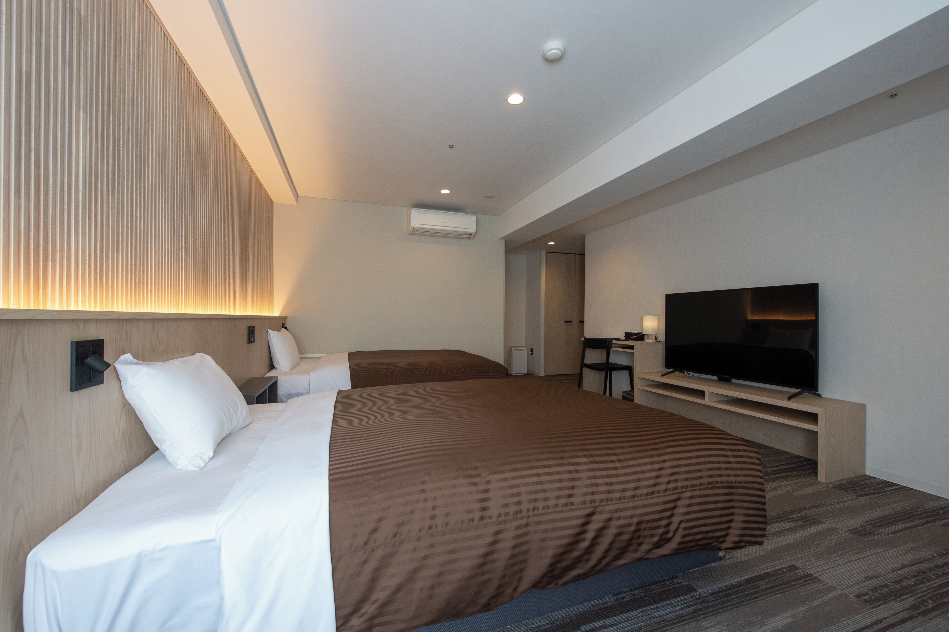 A modern hotel room with a large bed, a TV, and a desk area.