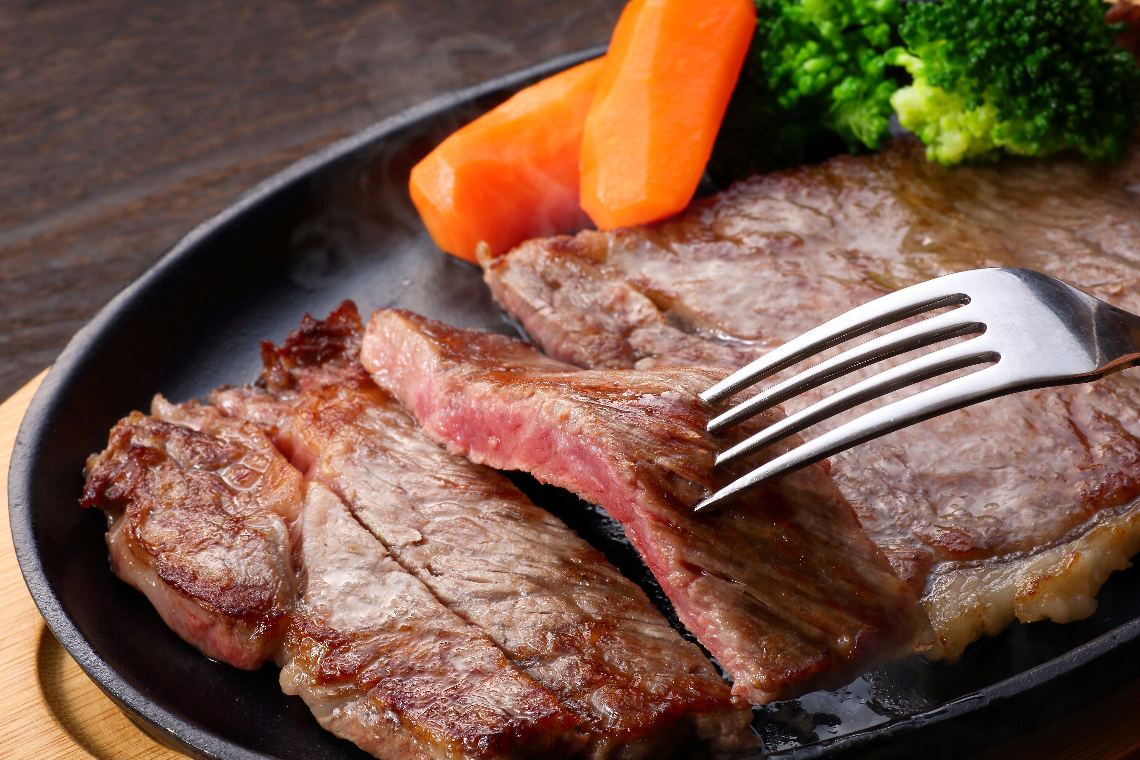 Ein Steak mit einer Gabel in einer Pfanne, serviert mit Brokkoli und Karotten.