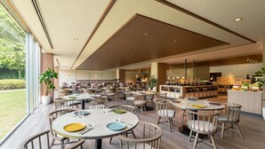 A spacious dining area with multiple round tables and chairs, a central bar area, and large windows offering a view of the outdoors. - Mercure Fukuoka Munakata Resort & Spa (Munakata)