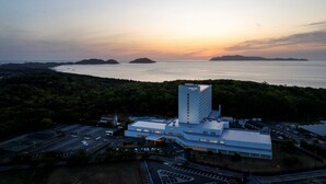 A modern hotel with a parking lot and a view of the sea during sunset. - Mercure Fukuoka Munakata Resort & Spa (Munakata)