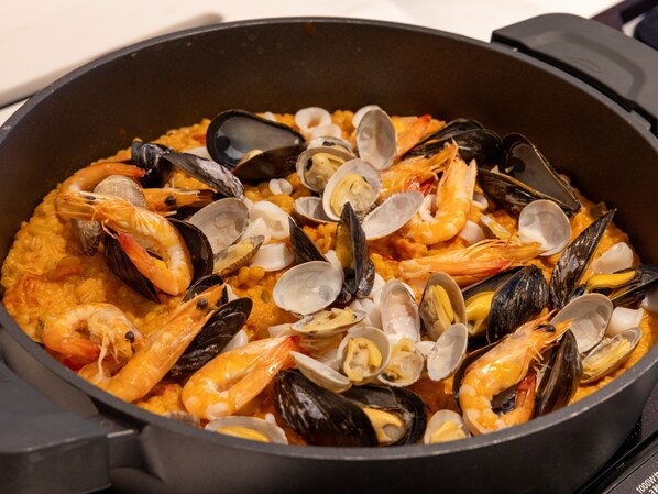 Una olla grande y negra llena de mariscos, como camarones y mejillones, en una cocina.