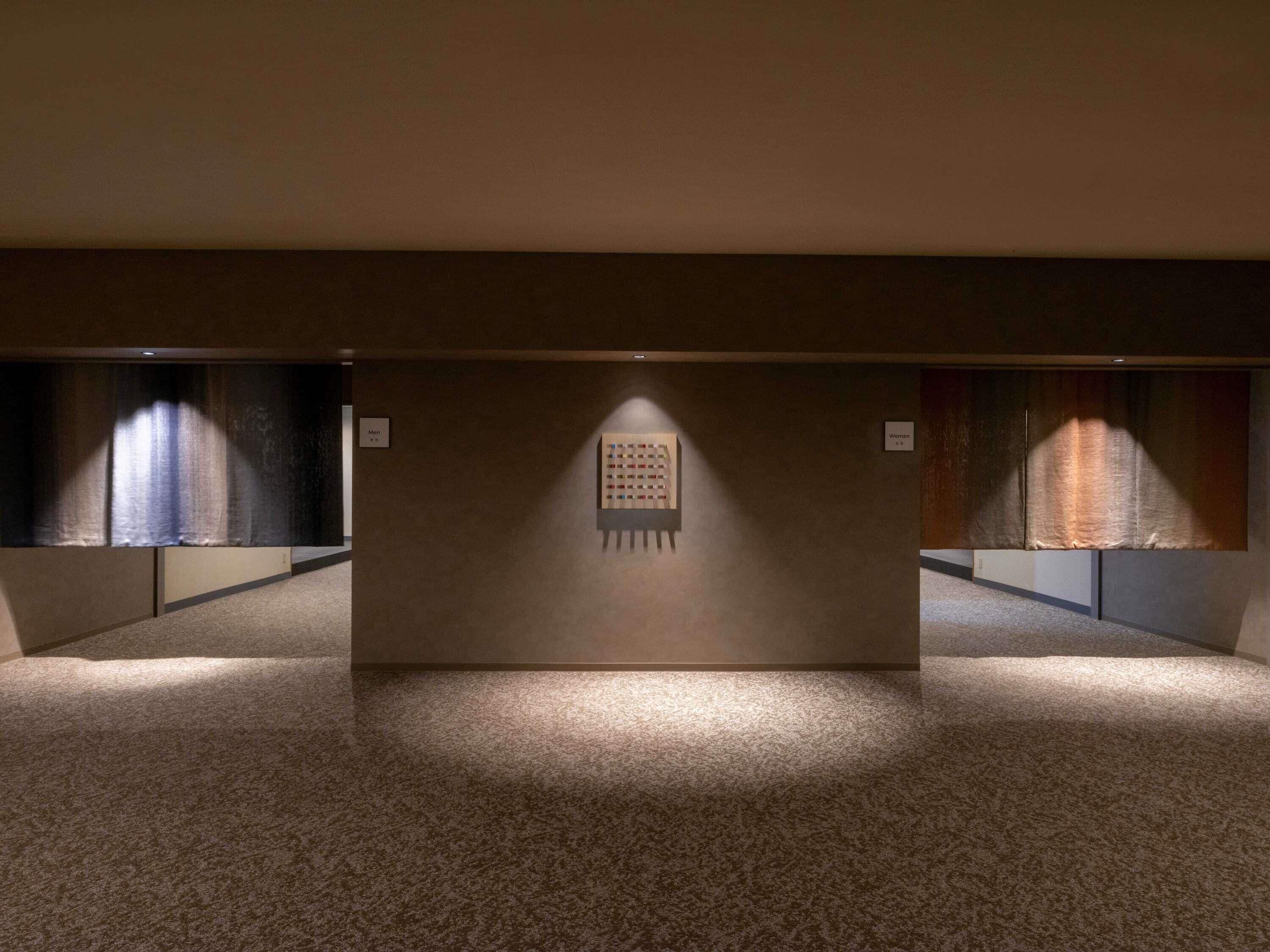 A hallway with carpeted floors and walls, featuring two signs labeled "Men" and "Women" indicating restroom locations.