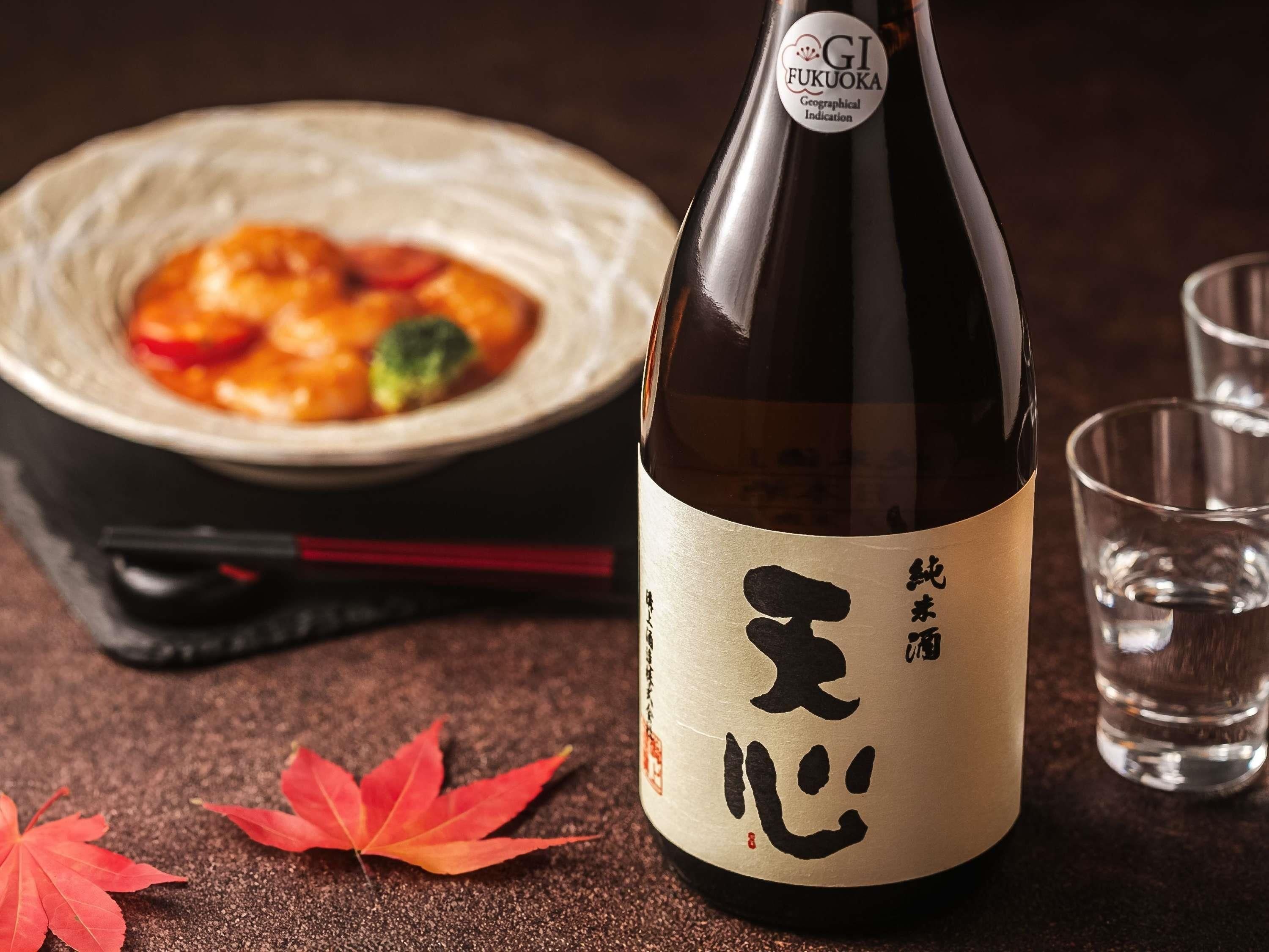A bottle of sake with a label, a bowl of food, and a glass of water on a table.