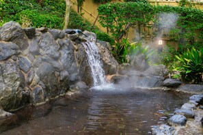 Una cascada de piedra en un jardín con un cerco de madera y follaje al fondo.