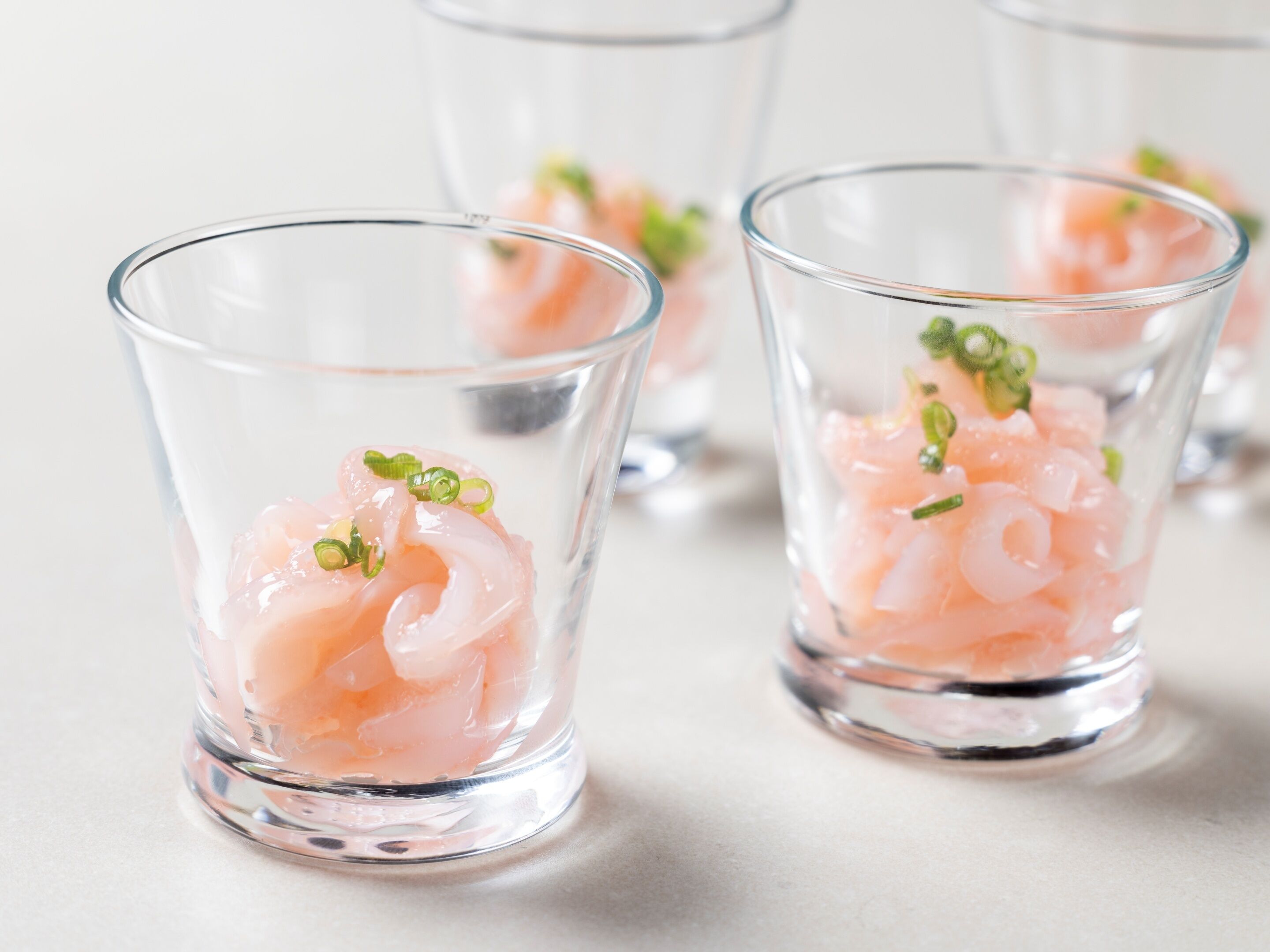 Three clear glasses containing pink shrimp and green onions.