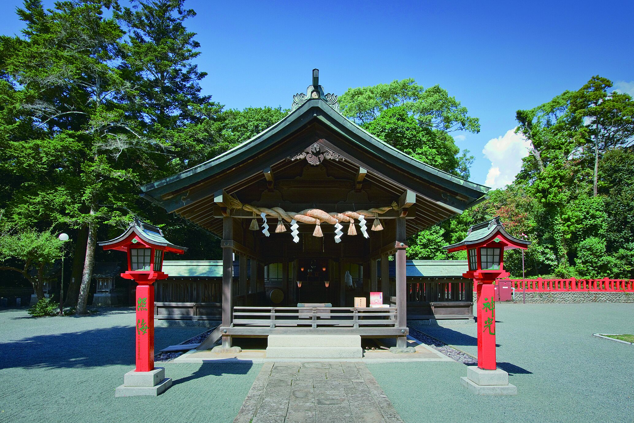 Une construction traditionnelle japonaise, dotée d’un toit vert et de piliers rouges, entourée d’arbres.