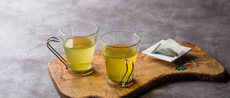 Two glasses of yellow tea on a wooden tray with a tea bag and a small tag.