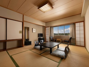 Una habitación tradicional japonesa con suelo de tatami, una mesa baja, sillas, un televisor y un gran ventanal con vistas.