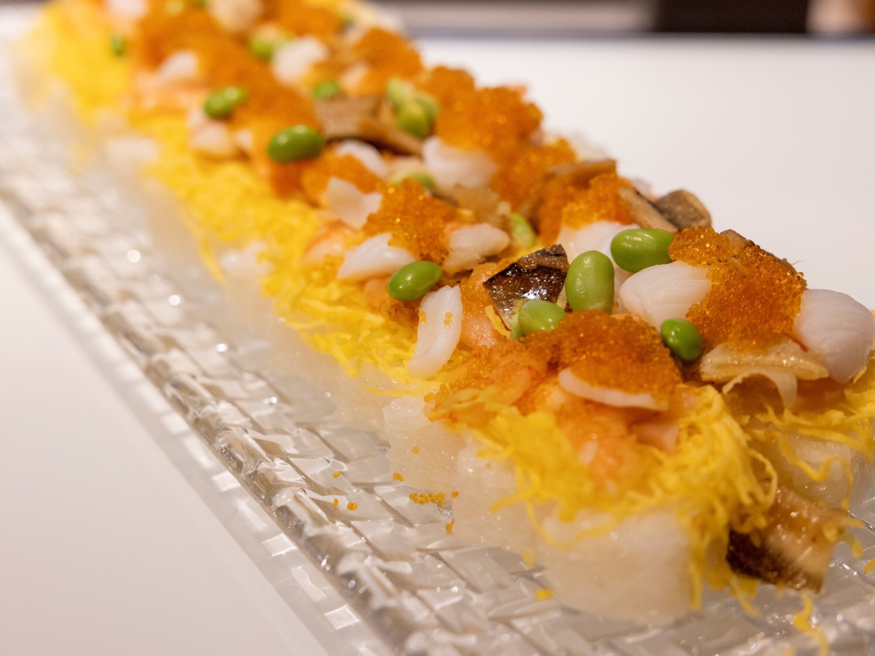 A sushi dish with shrimp, fish, and green peas on a clear glass plate.