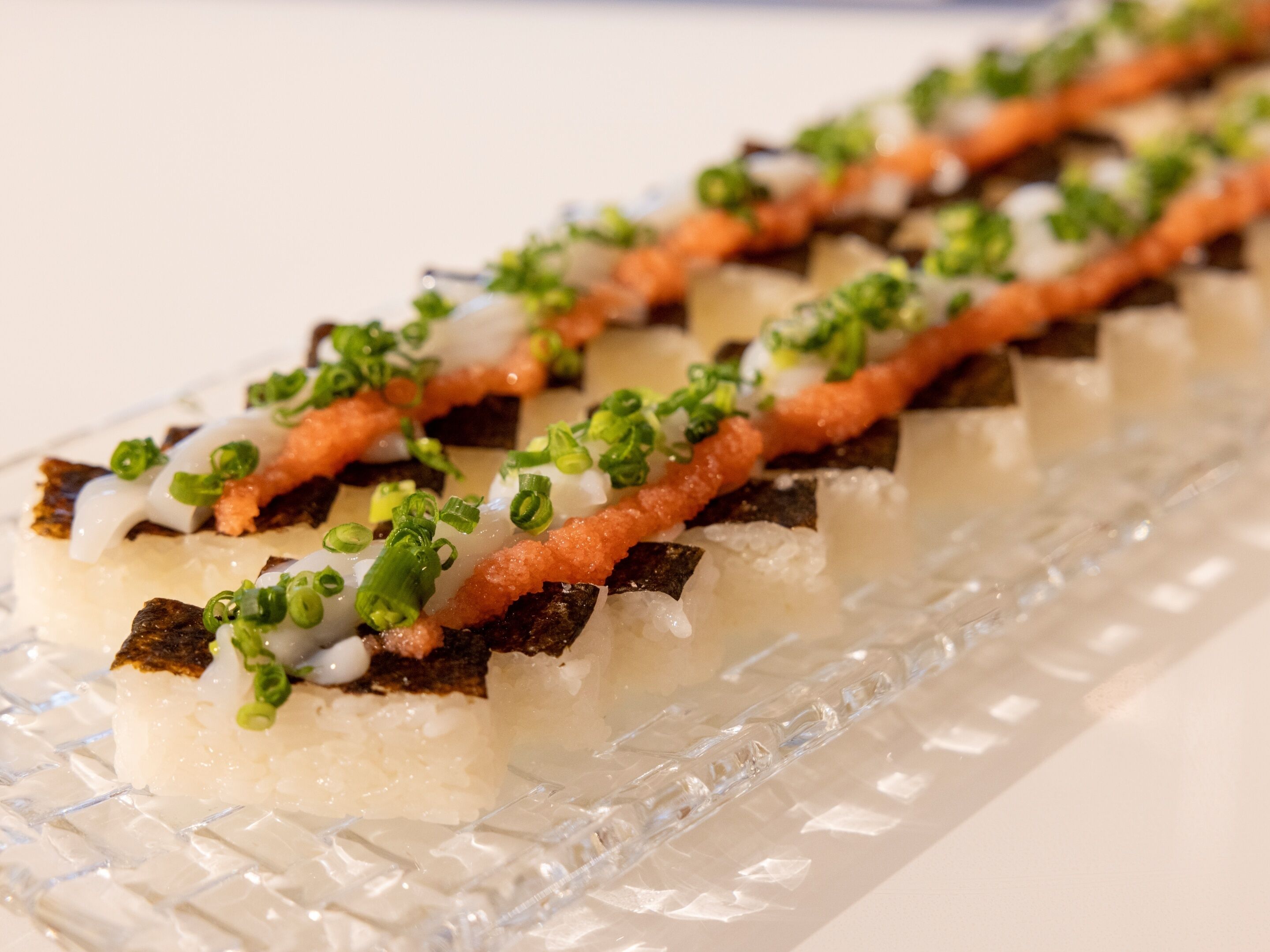 Een sushi gerecht met rijst, vis en garnering op een glazen bord.