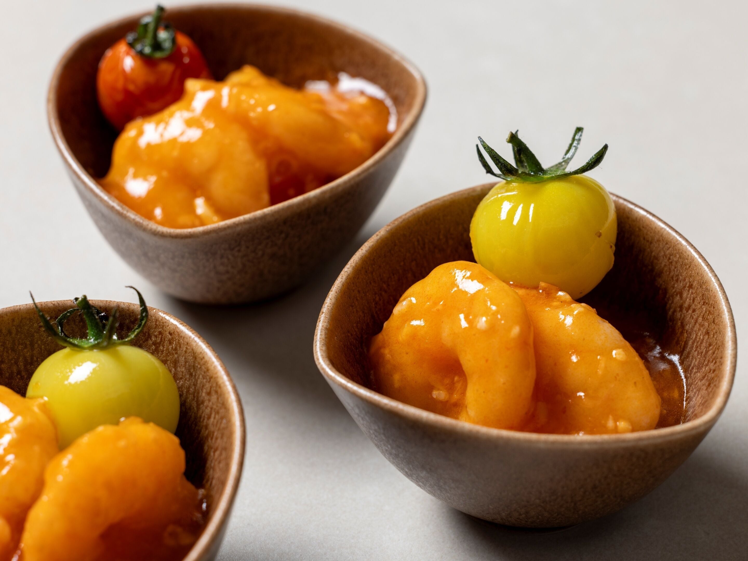 Tres tazones con fruta glaseada y un tomate cherry.