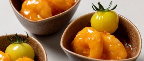 Three bowls containing glazed fruit and a cherry tomato.