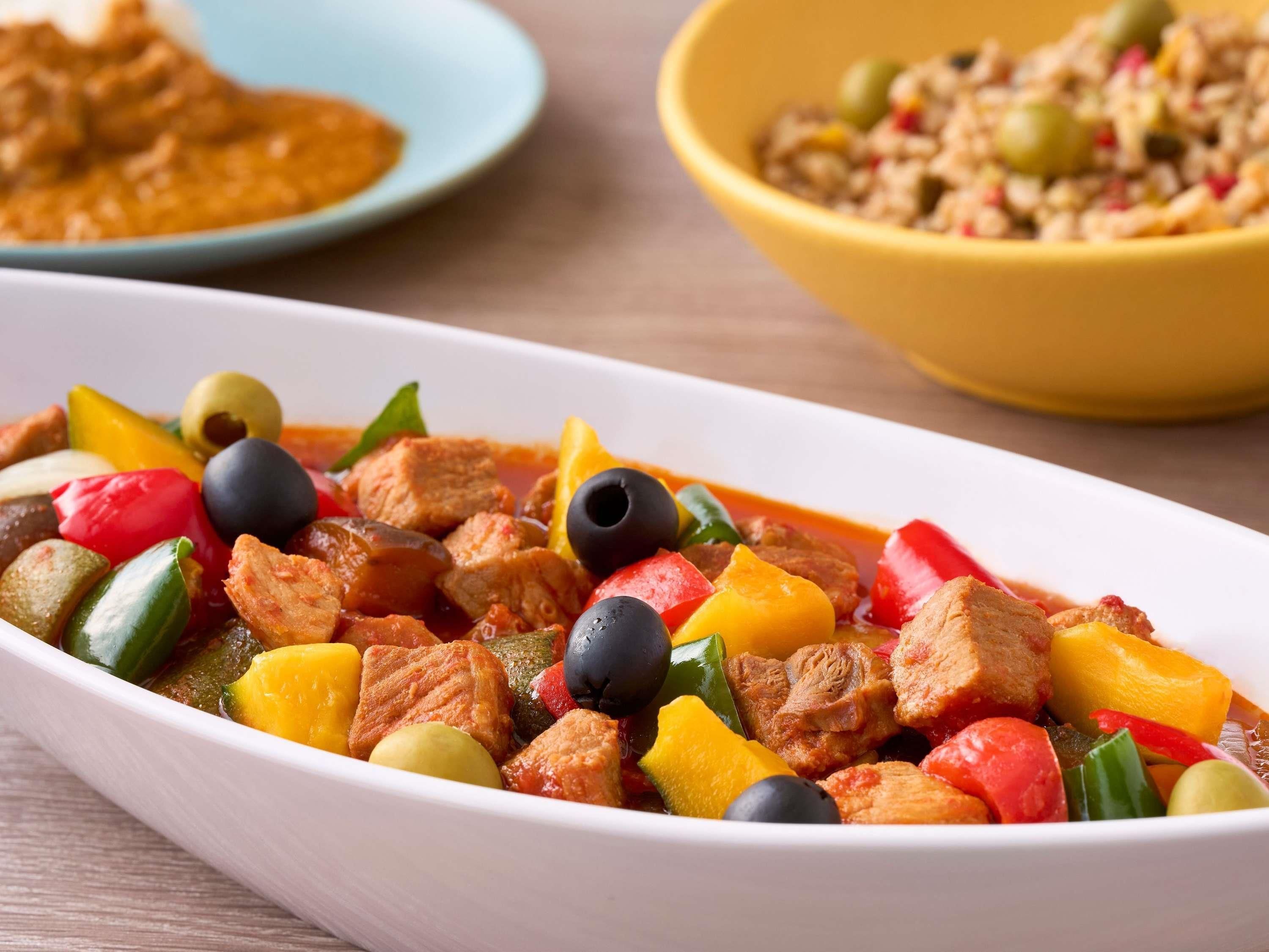 A dish with meat, vegetables, and olives.
