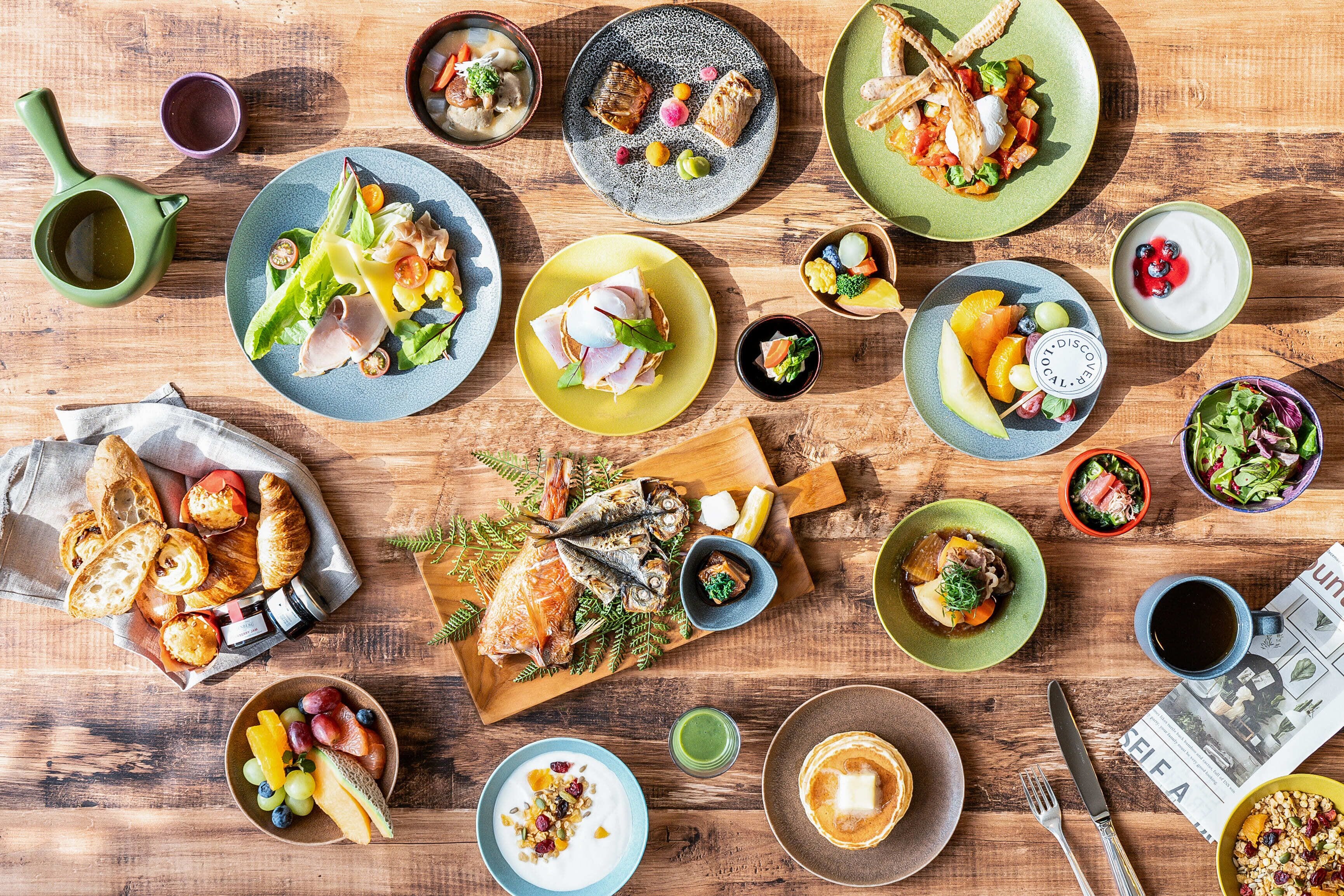 Una mesa de madera con varios platos, incluyendo pescado, ensaladas y frutas, que sugiere un ambiente para comer.