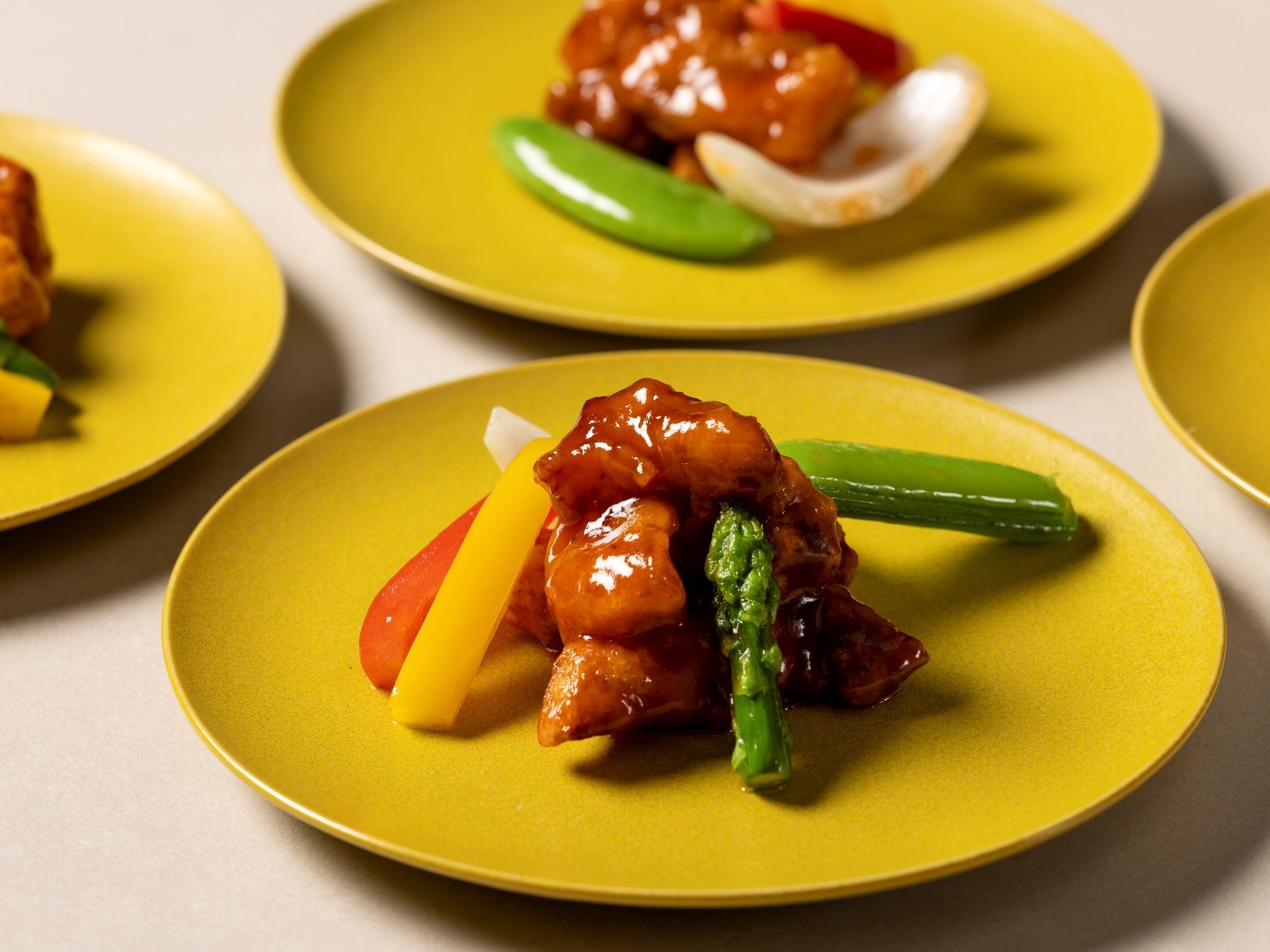 A close-up of a dish with glazed chicken and vegetables on a yellow plate.