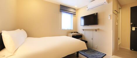 A hotel room with a bed, a desk, a flat-screen TV mounted on the wall, and an air conditioning unit.