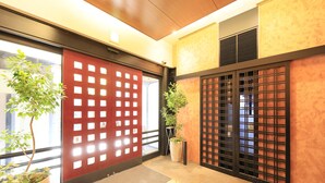 A hallway with a red sliding door, a potted plant, and a tiled floor. - Hotel Nihonbashi Saibo (Tokyo)