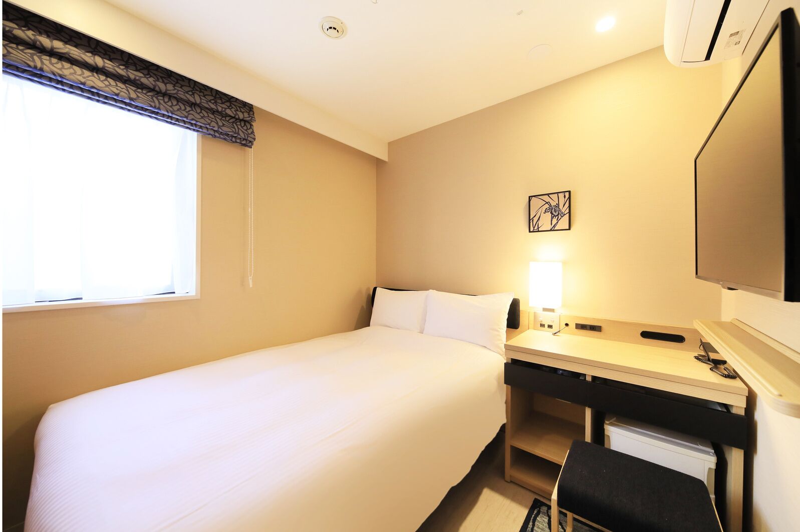 A hotel room with a bed, a desk with a chair, a television, and a window with curtains.