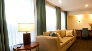 A hotel room with a sofa, a table with a lamp, a chair, and a desk. - El Cielito Hotel (Makati)